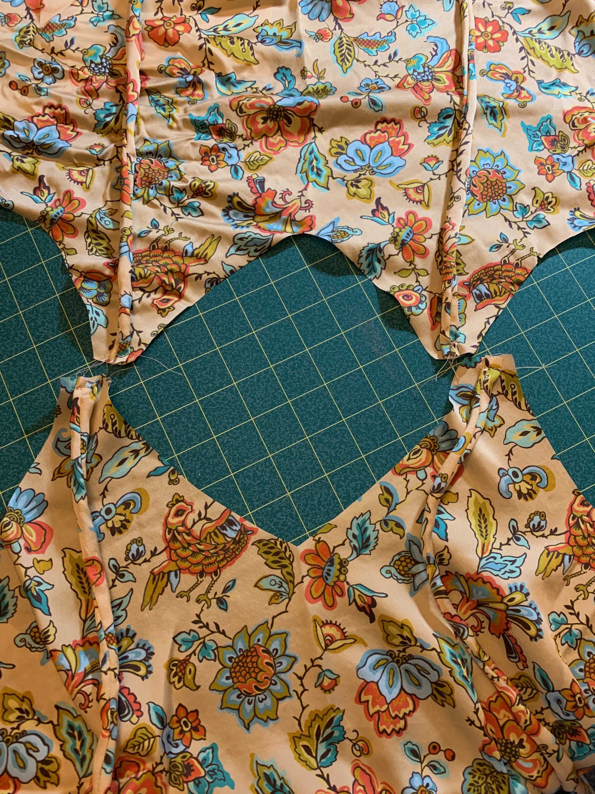 Colorful floral patterned fabric pieces cut into shapes, laid on a green grid cutting mat, with warm tan, orange, and blue tones.